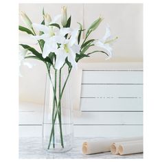 some white flowers in a clear vase on a marble counter top next to rolled up paper