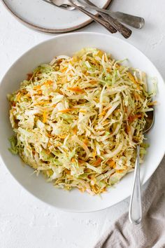 a white bowl filled with coleslaw on top of a table next to silverware