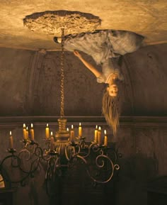 a woman with long hair is suspended from a chandelier in a dark room