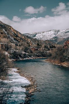 a river flowing through a lush green forest covered hillside next to a snow covered mountain