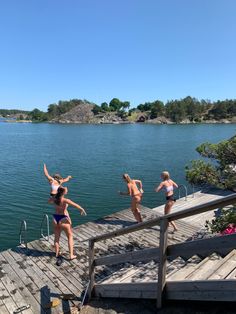 four young women are jumping off the dock into the water while another woman is on the other side of the dock