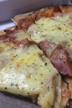 a pizza with ham and cheese on it sitting in a box next to a fork