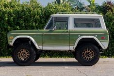 an old green truck parked in front of a hedge