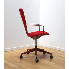 a red office chair sitting on top of a hard wood floor next to a white wall