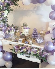 a table with purple and white balloons, cake and flowers on it in front of a mirror