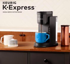 a coffee maker sitting on top of a wooden table next to a cup and mug