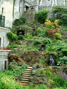 a stone building with lots of plants and flowers on the steps leading up to it