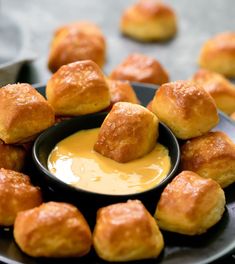 a black plate topped with rolls covered in cheese and dipping sauce next to other rolls