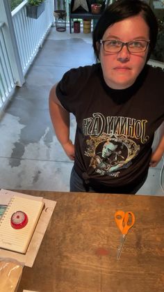 a woman wearing glasses standing in front of a table with scissors and cutting paper on it