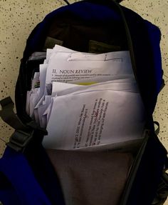 an open blue backpack filled with papers on top of a floor next to a wall