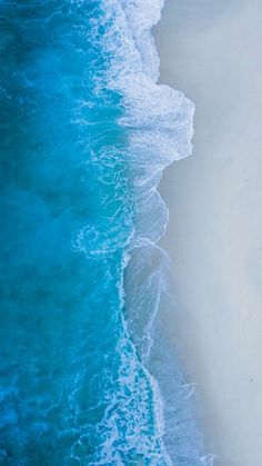 an aerial view of the ocean with waves crashing on the shore and people walking along the beach