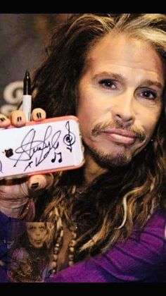 a man with long hair holding up a cell phone in front of his face and writing on it