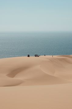 people are walking across the sand dunes by the ocean