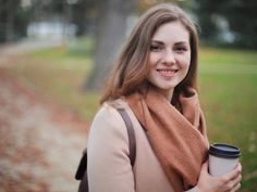 a woman is holding a coffee cup and smiling at the camera while standing in front of a path