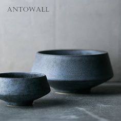 two black bowls sitting next to each other on top of a gray tablecloth covered floor