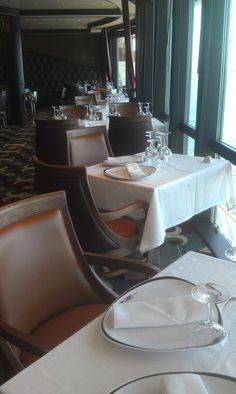 a dining room with white table cloths and brown leather chairs in front of large windows