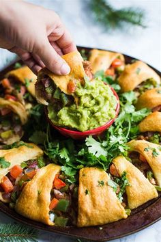 a person dipping guacamole into a bowl filled with food