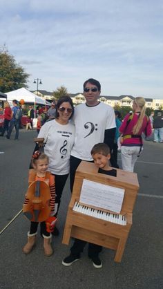 a man, woman and two children are standing in front of an organ with sheet music on it