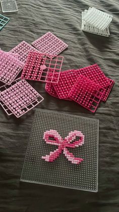 several pieces of pink and white art made out of legos sitting on a bed