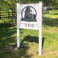 a white sign sitting in the middle of a grass covered field next to a fence