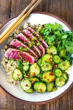 a white plate topped with meat, rice and cucumbers next to chopsticks