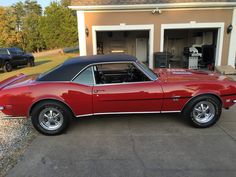 a red car is parked in front of a garage with its hood up and the door open