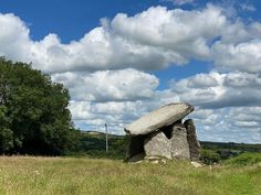 a large rock sitting on top of a lush green field under a cloudy blue sky