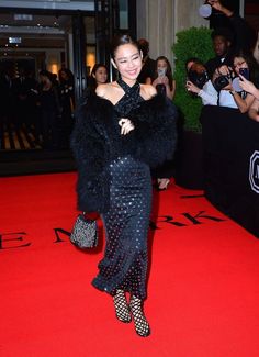 a woman in a black dress and fur coat walking down a red carpeted area