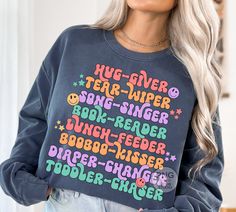 a woman with blonde hair wearing a sweatshirt that reads hug - giver, tear - wiper, boom - reader, boun - feeder, boobob - ringer, and bubble - rings