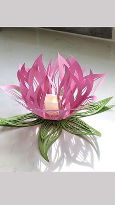 a pink flower sitting on top of a table next to a lit candle in it