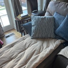 a couch with several pillows on it in front of a window and a book shelf