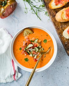 a bowl of tomato soup with bread on the side and garnished with fresh herbs