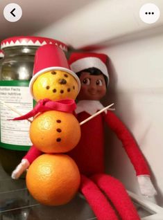 an elf with a snowman made out of oranges on top of a shelf