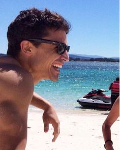 a man laughing on the beach with his jet ski in the background