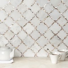 a white tea pot sitting on top of a counter next to cups and saucers