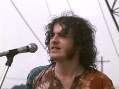 a man standing in front of a microphone with long hair and wearing a tie dye shirt