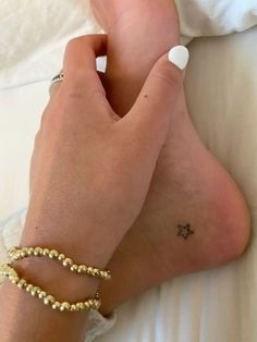 a woman's foot with a small star tattoo on her left ankle and gold beaded bracelet