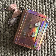 a pink bow is on top of a holographic book with buttons and pins