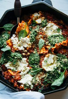 a skillet filled with pasta and spinach covered in sauce, cheese and herbs