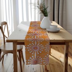 an orange table runner on top of a wooden table with two chairs and a vase