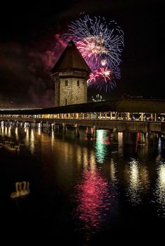 fireworks are lit up in the night sky above a bridge and river with water reflections