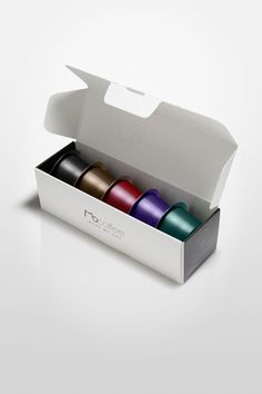 an open box with four different colored spools in it on a white surface