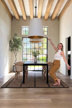 a woman standing in front of a dining room table with her arms up and legs spread out