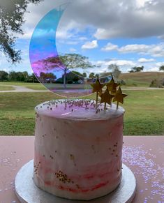 a pink cake with stars on top sitting on a table in front of a park