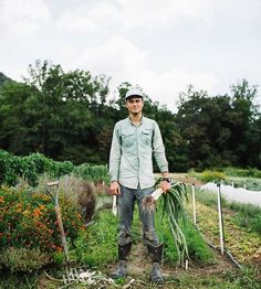 a man standing in the middle of a garden holding two shovels and some plants