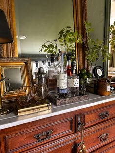 a dresser with bottles and candles on top of it next to a mirror, lamp and potted plant