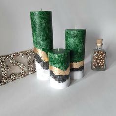 three green candles sitting on top of a table next to a bottle and bead