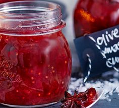 a jar filled with red liquid sitting on top of a table next to an apple