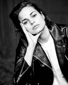 a black and white photo of a woman with her hand on her chin wearing a leather jacket