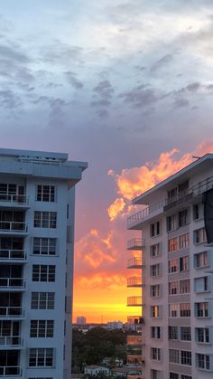 the sun is setting over some buildings in front of a building with balconies